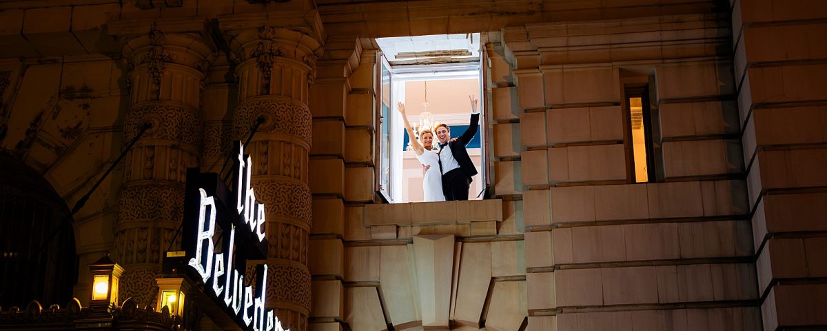 Bride and groom look excited about being married in an upstairs window