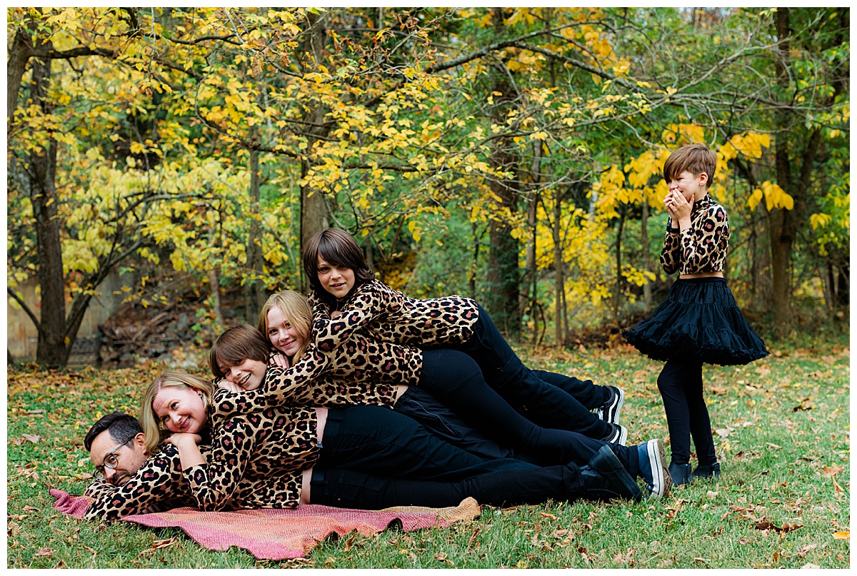 Family piles on top of each other for their awkward family photos in Baltimore with the fourth and youngest child standing to side, not sure how to get on top. 