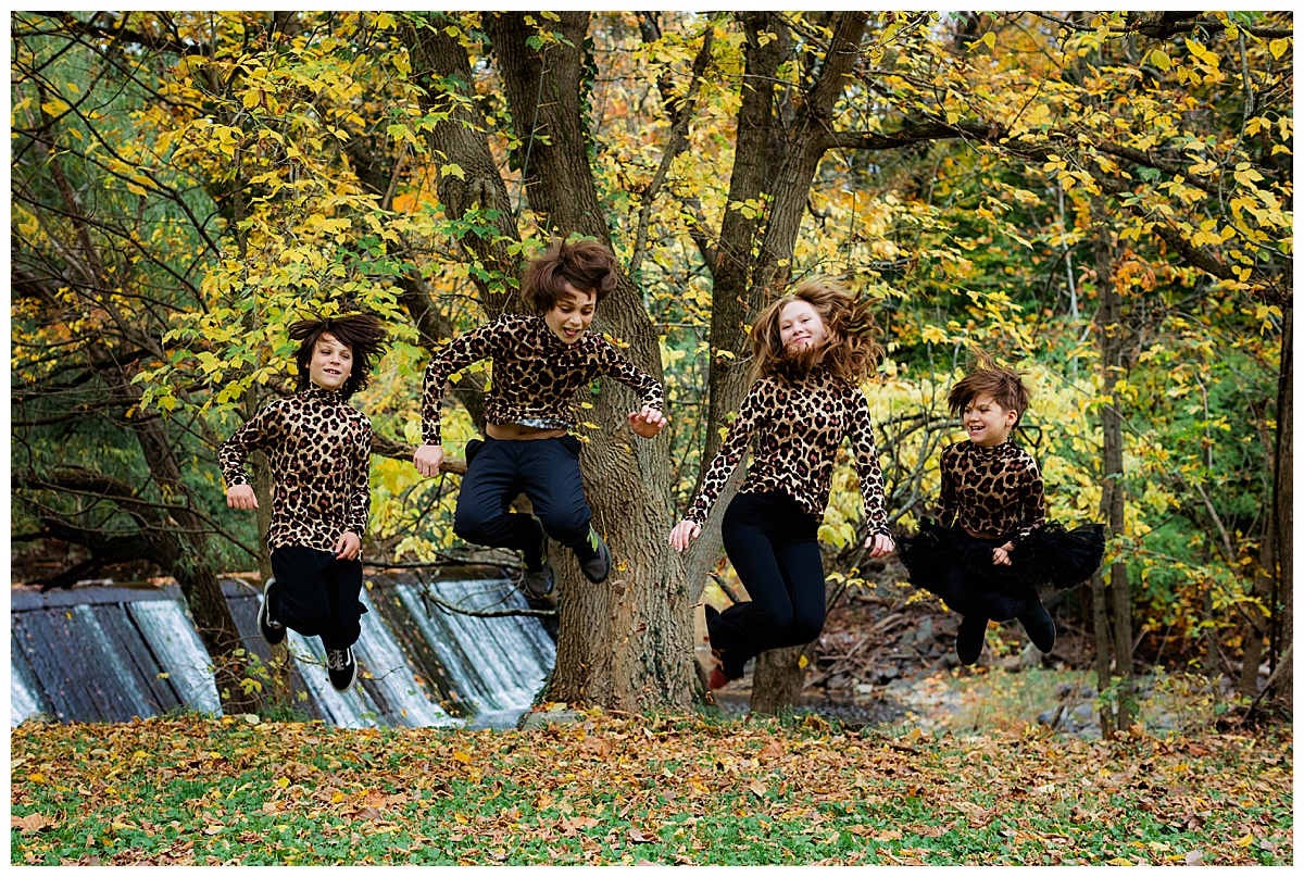 Siblings jump as high as they can in the air in their matching leopard outfits.
