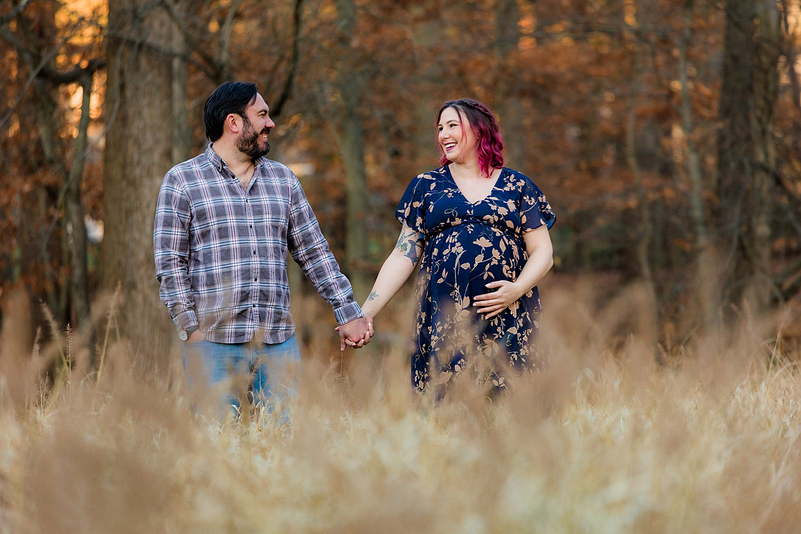 Maternity couple holds hands in a field in the backyard of their neighborhood in Maryland.