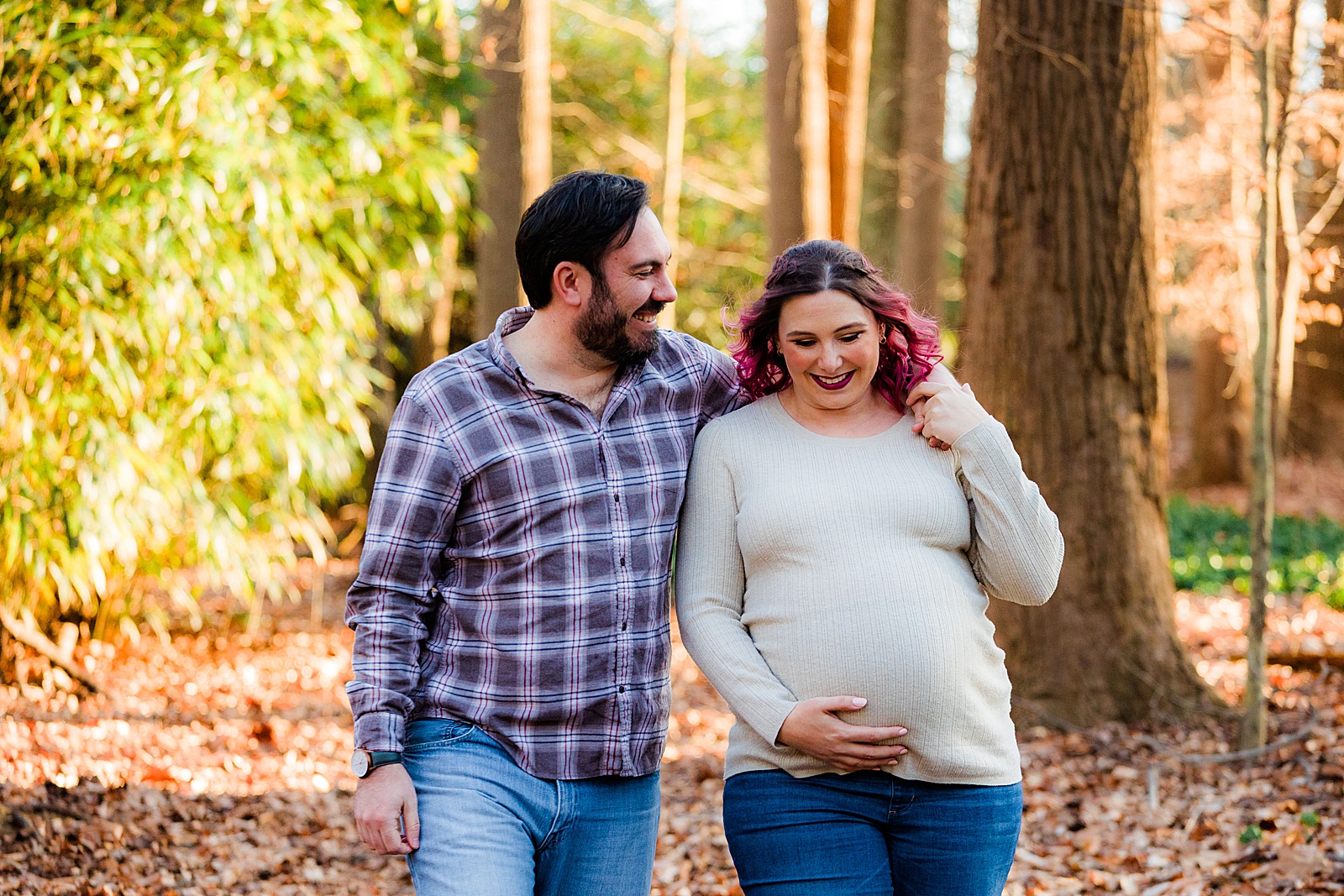 Married couple walks through backyard forest while holding pregnant belly.