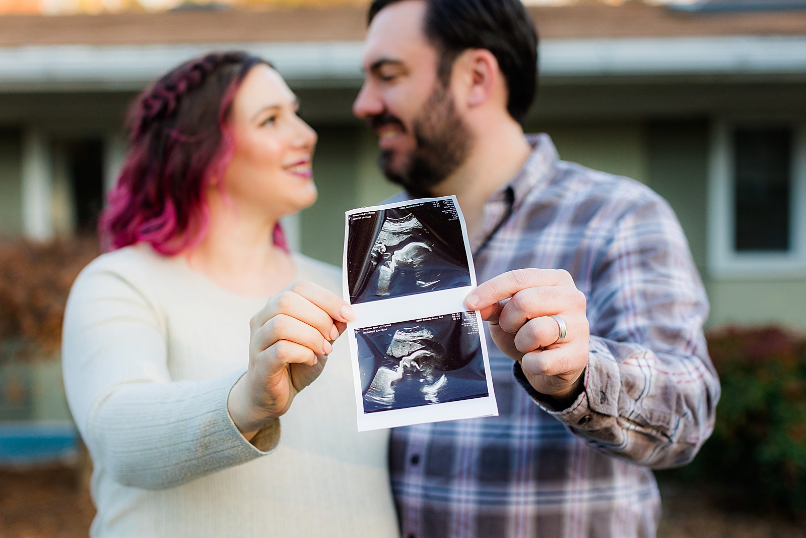 Couple holds ultrasound photo of baby at their maternity shoot outside their home. 