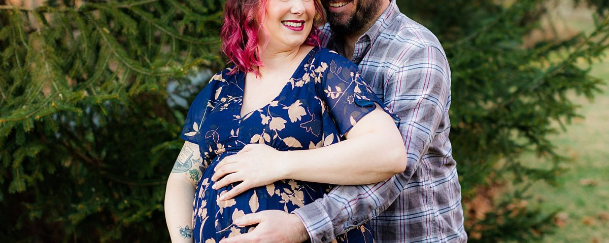 Husband hugs wife from behind and all hands cover her pregnant belly.