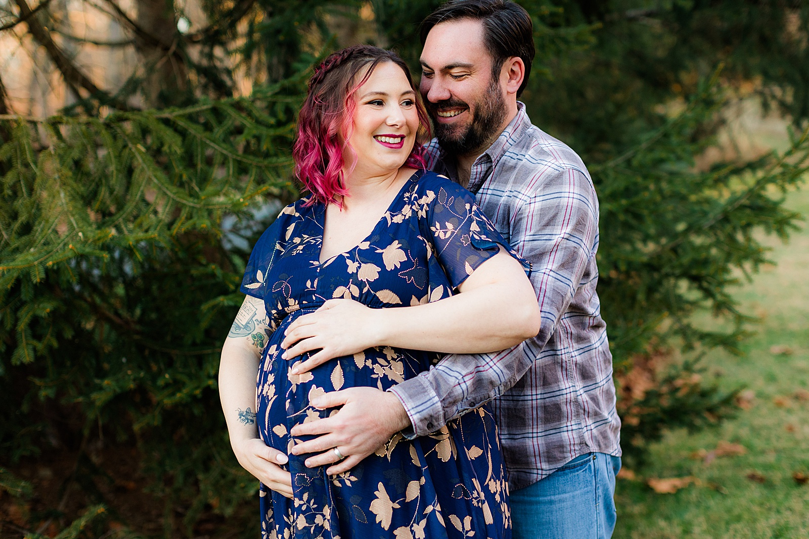 Husband hugs wife from behind and all hands cover her pregnant belly. 