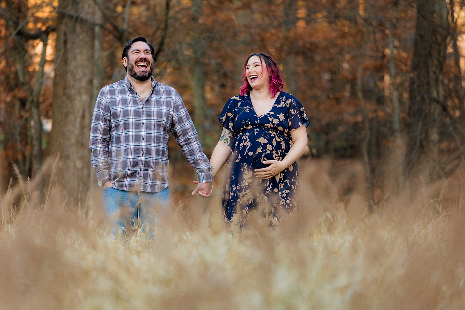 Couple laughs while standing in a backyard field for their maternity session.