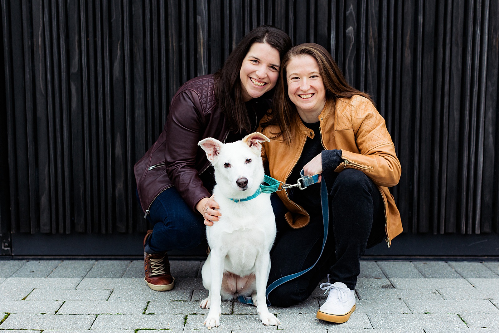 LGBTQ couple poses with their dog against a black textured wall for their Eckington DC engagement photography session.