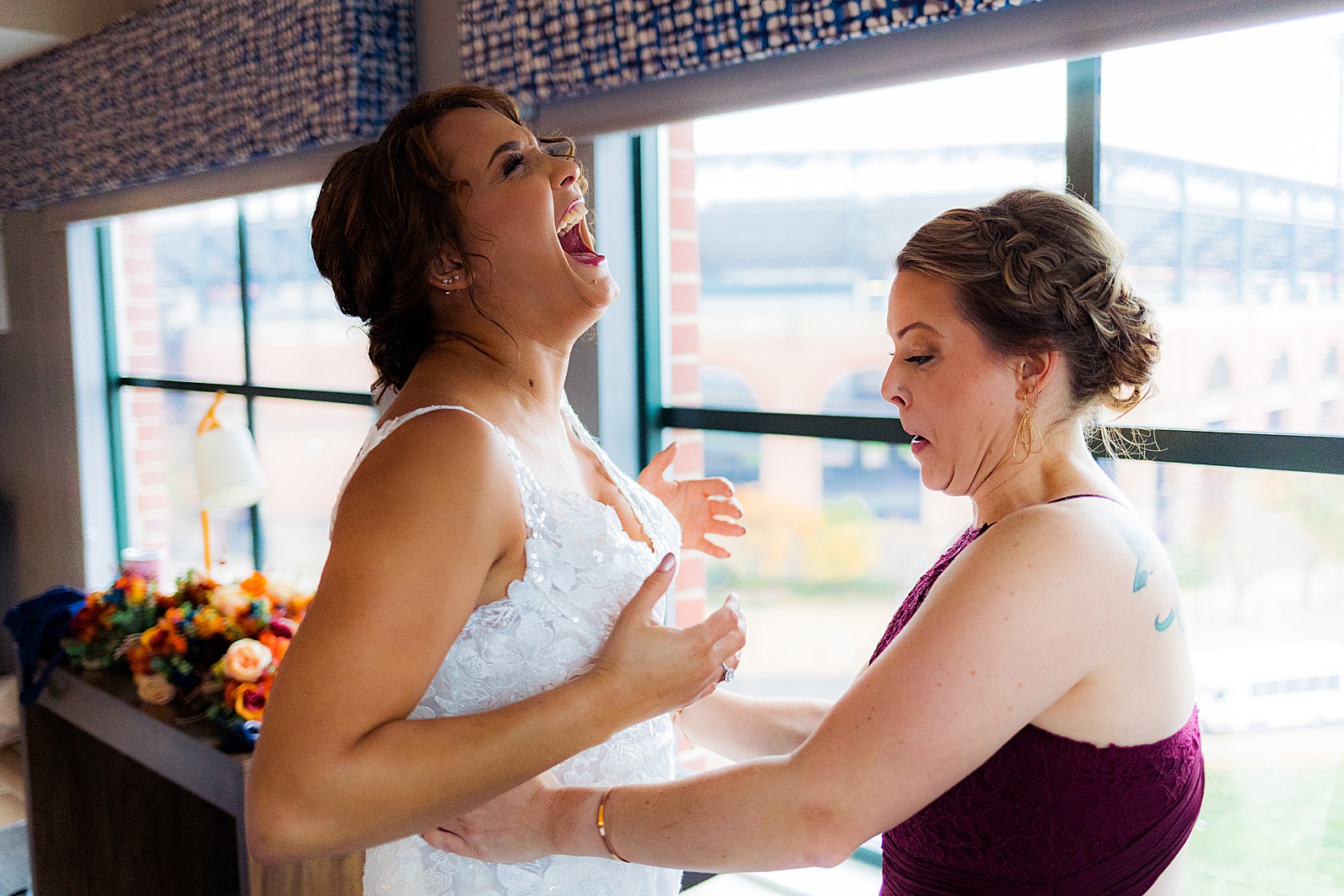 Bridesmaid helps bride fit into her dress as she gets ready. 