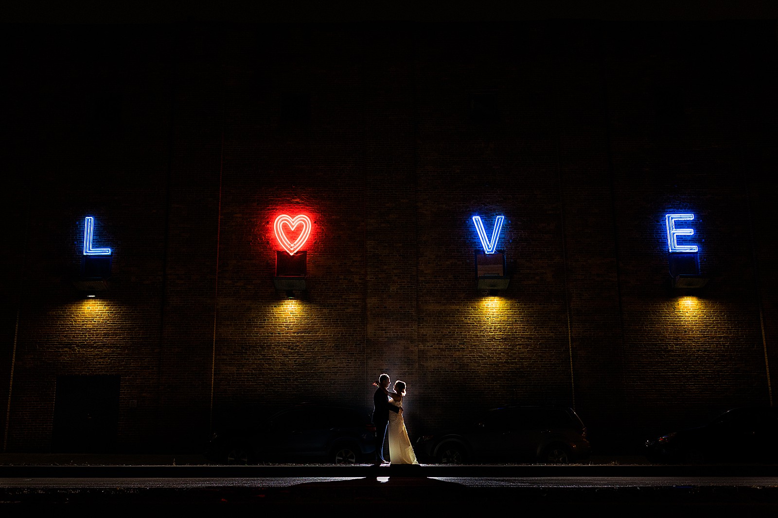 Bride and groom pose for a backlit outdoor night shot in front of the love sign at the American Visionary Art Museum in Baltimore. 