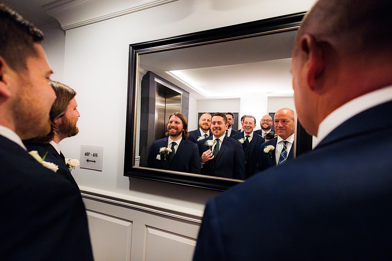 Groom and groomsmen check themselves out in a mirror. 