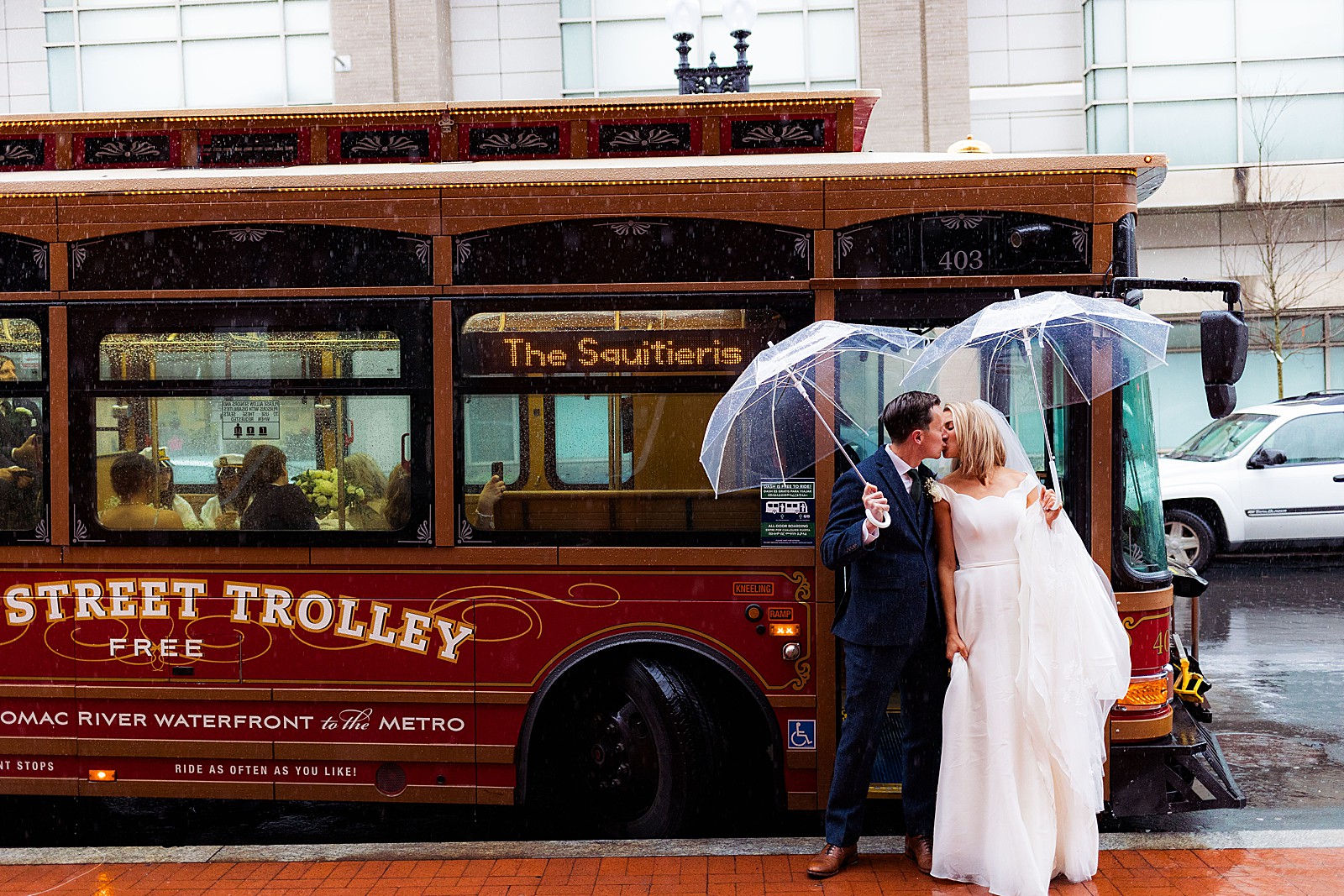 Bride and groom kiss under umbrellas outside of their trolley to take them to the Mount Vernon Inn Restaurant on their rainy wedding day.