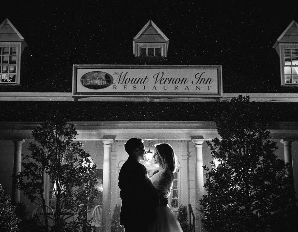 Bride and groom stand in front of the front of the Mount Vernon Inn Restaurant in a misty rain at night.